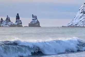 Vikurfjara black sand beach with clear view of snow covered Reynisdrangar on a winter day in Iceland.