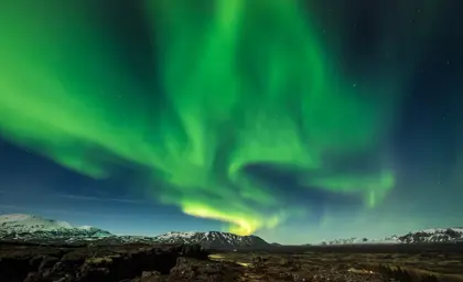 Northern lights at Þingvellir National Park reaching over mountain range in the background.