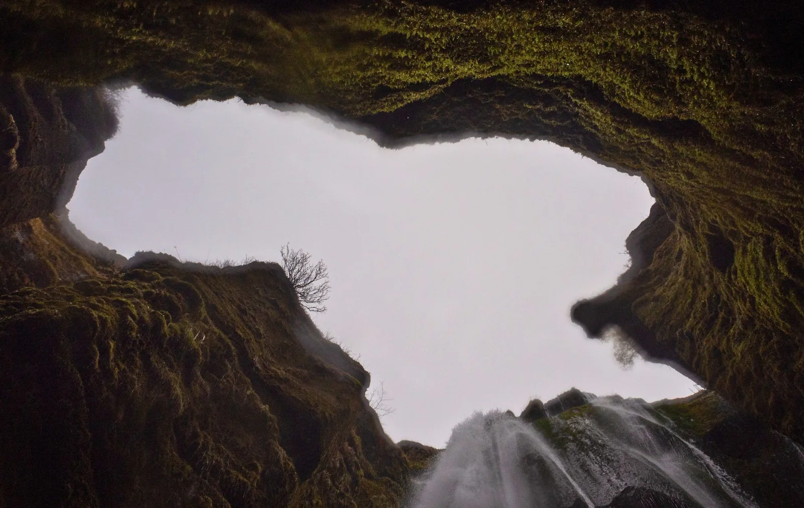 View looking up through the narrow mossy canyon toward the sky above Gljúfrabúi Waterfall’s hidden chamber.