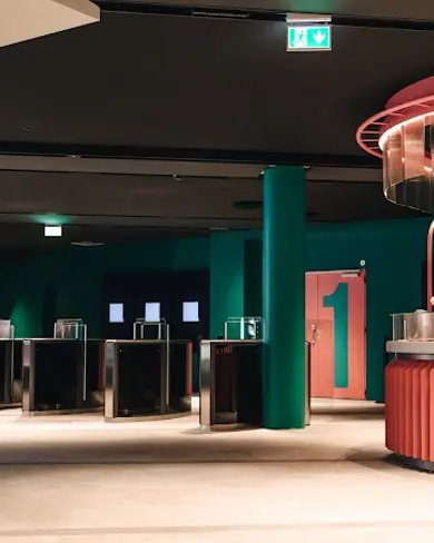 Interior view of Sambíóin Kringlan cinema in Reykjavík, featuring modern design with green walls, pink counters, and ticket gates, offering a stylish movie-going experience.
