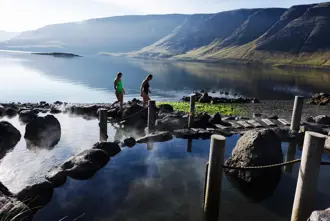 Hvammsvik hot springs in Iceland with mountain views and guests walking by.