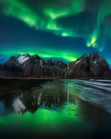 Northern Lights shining brightly over Vestrahorn mountain in Iceland, featured as a banner for Travel Reykjavik's tour promotions.