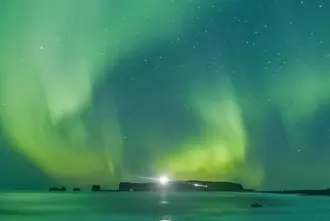 Reynisfjara Black Sand Beach with Northern Lights in Green dancing above on a dark winter night in Iceland.
