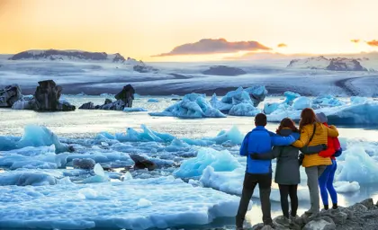 A group of travelers on a private glacier lagoon tour admiring the breathtaking Jökulsárlón Glacier Lagoon at sunset, with massive icebergs floating in the serene water under a golden sky in Iceland.