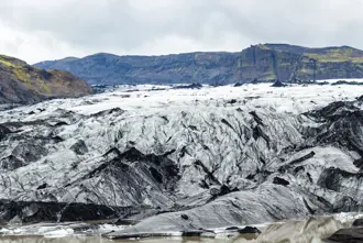 Close-up of Sólheimajökull Glacier in Iceland, featuring a rugged mix of white ice and black volcanic ash under cloudy skies, showcasing the glacier's dramatic landscape.