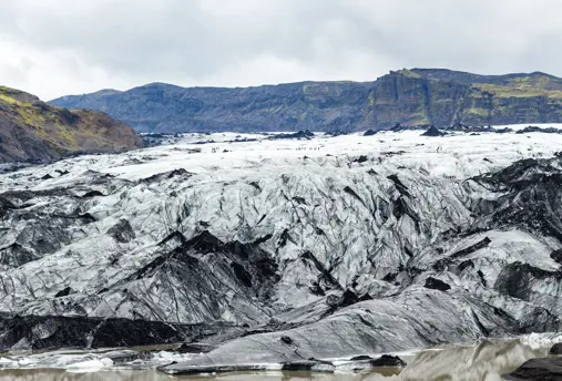 Close-up of Sólheimajökull Glacier in Iceland, featuring a rugged mix of white ice and black volcanic ash under cloudy skies, showcasing the glacier's dramatic landscape.
