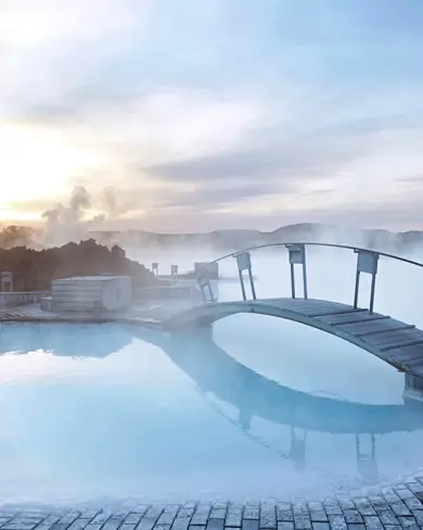 Misty sunrise at Blue Lagoon Iceland with steam rising over the geothermal spa and a wooden bridge reflecting in the tranquil blue waters.