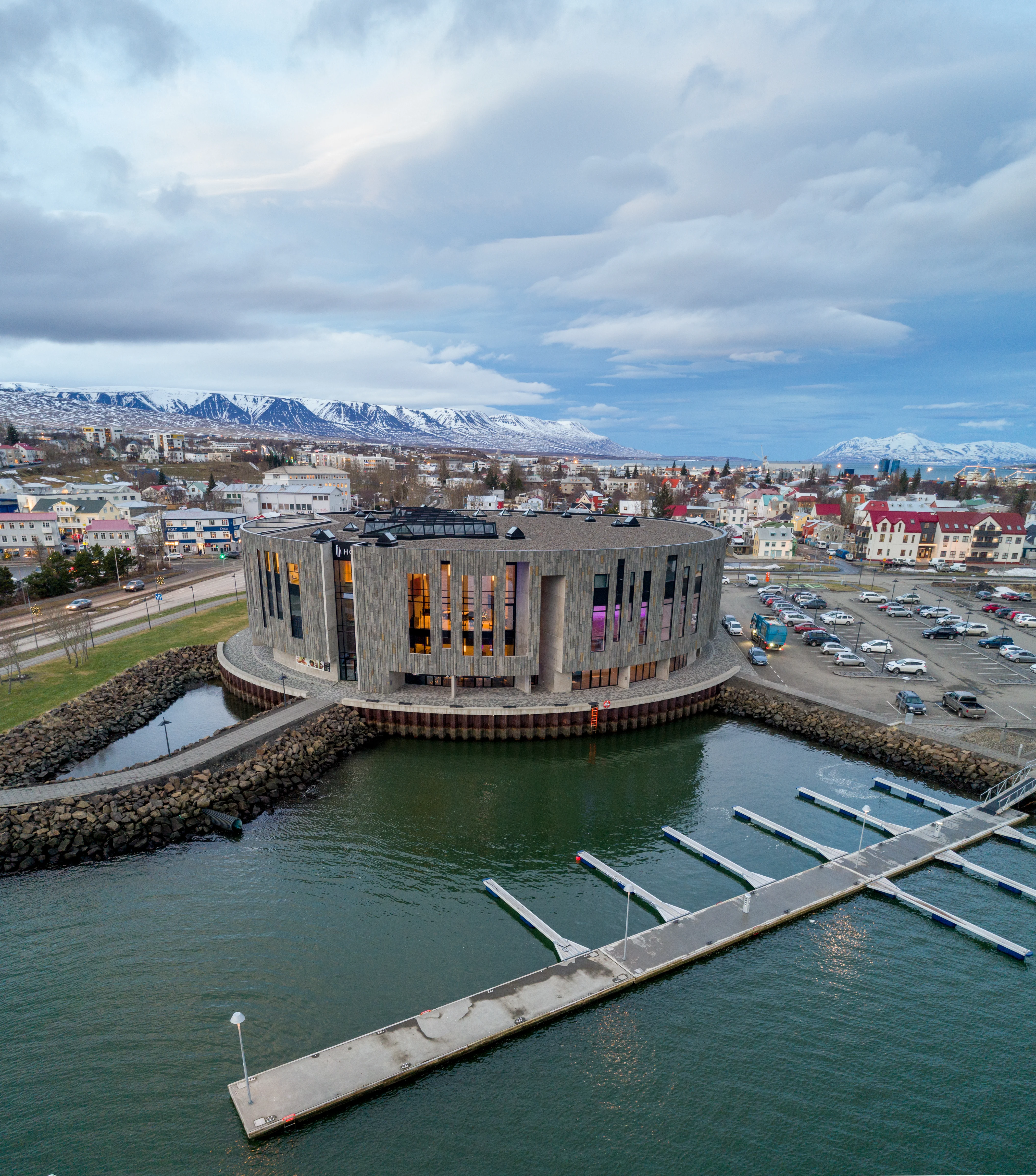 Hof Cultural and Conference Center in Akureyri, a modern building by the waterfront, with snow-capped mountains and the town’s skyline visible in the background.