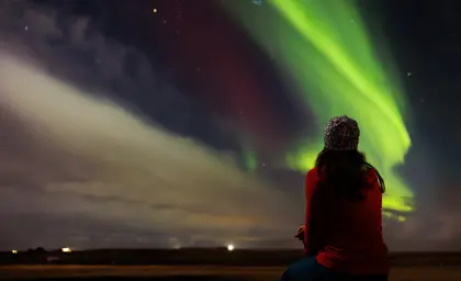 Woman in red standing under the northern lights and starry sky on a 5 day northern lights tour in Iceland.