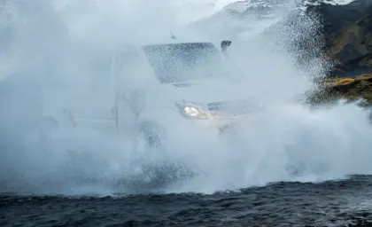 A white superjeep from Travel Reykjavík drives through a river in the Icelandic highlands, creating an impressive splash of water during a private 4x4 tour.