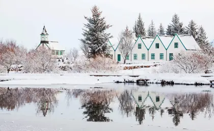 Charming snow-covered church and houses in Thingvellir National Park, Iceland, with their reflections shimmering in a frozen lake.