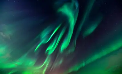 Close up view of the northern lights in Iceland, with bright green colors dancing across the night sky, illuminating the dark horizon