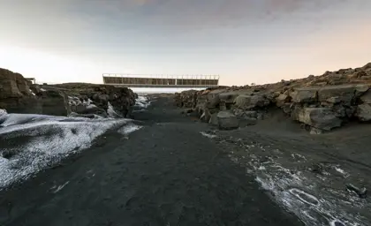 View of the Bridge Between Two Continents in Iceland at sunset, showcasing the dramatic landscape of black sand, rugged rocks, and the symbolic footbridge connecting the Eurasian and North American tectonic plates.