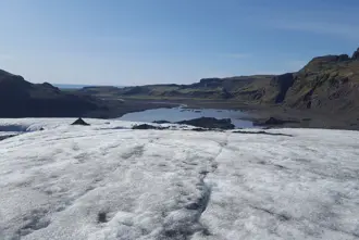 View from Sólheimajökull Glacier looking over a glacial lake and surrounding mountains, illustrating Iceland's striking natural landscapes under clear blue skies.