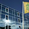 The glass exterior of Hótel Edda in Akureyri with the hotel's easily recognizable yellow flag raised under a blue sky.