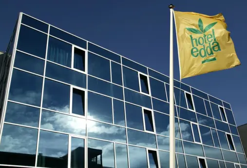 The glass exterior of Hótel Edda in Akureyri with the hotel's easily recognizable yellow flag raised under a blue sky.