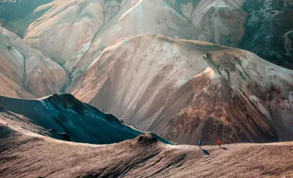 Two hikers walking along the crest of a rhyolite mountain ridge in Landmannalaugar with multicolored slopes in the Icelandic highlands.