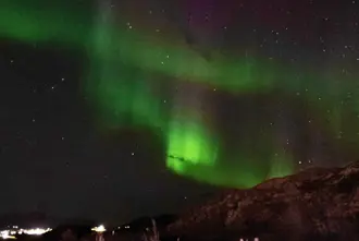 Bright green northern lights over Akureyri dancing in a pitch black winter sky.