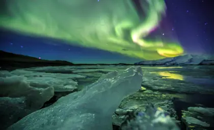 Mesmerizing view of the Northern Lights reflecting on the icebergs at Jökulsárlón Glacier Lagoon.