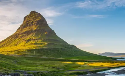 Scenic view of the Snæfellsnes Peninsula in Iceland with Kirkjufell mountain bathed in warm sunlight with lush green surroundings and the sea in the background.