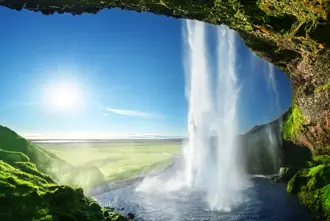 Majestic summer view from behind Seljalandsfoss Waterfall, on Iceland's five day guided tour, with bright sunlight illuminating the green landscape.