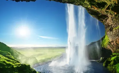 Majestic summer view from behind Seljalandsfoss Waterfall, on Iceland's five day guided tour, with bright sunlight illuminating the green landscape.