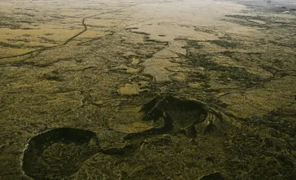 A scenic wooden boardwalk meandering through the colorful geothermal area of Seltún in Iceland, with steam vents and rugged terrain visible under an overcast sky.