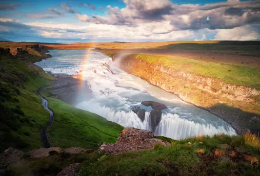 A rainbow arches over the powerful Gullfoss waterfall on a sunny day in Iceland's Golden Circle.