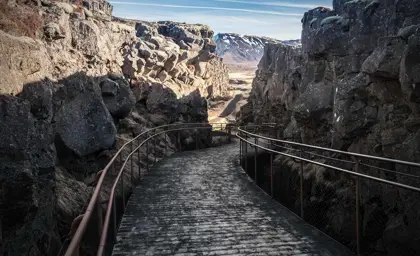 Thingvellir National Park walkway winding through volcanic rock formations under a clear blue sky, showcasing Iceland's stunning natural beauty and geological history.