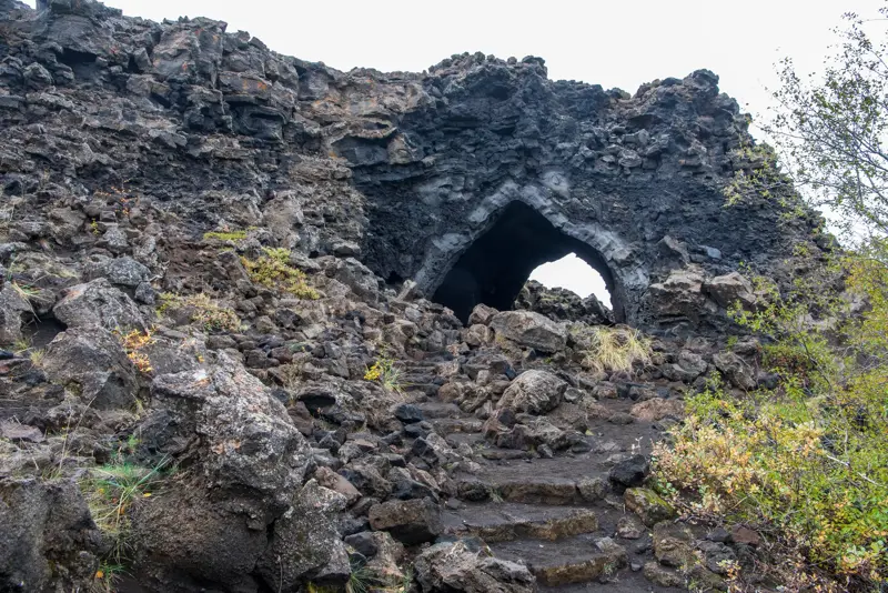 The church at Dimmuborgir lava field in Mývatn. A natural lava rock arch in Iceland, surrounded by rugged volcanic rocks and autumn foliage.