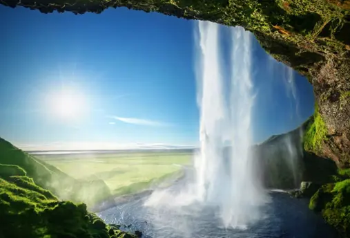 Seljalandsfoss waterfall in southern Iceland viewed from behind, with sunlight shining through the mist.