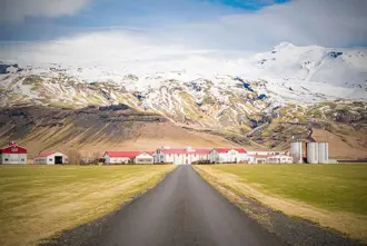 A scenic farm at the base of Eyjafjallajökull volcano in Iceland, surrounded by snow-covered mountains.