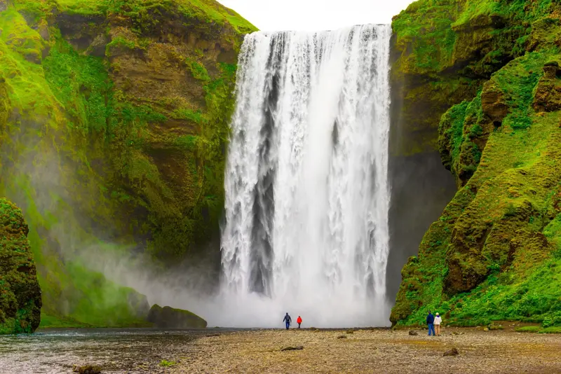 Skógafoss Waterfall cascading powerfully in Iceland, surrounded by lush green cliffs with tourists standing at its base.