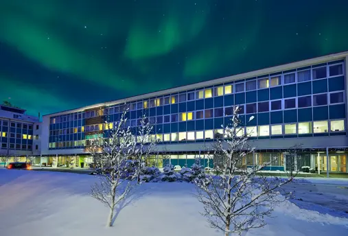 Berjaya Reykjavík Natura Hotel exterior view under the northern lights in the winter sky.