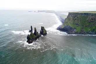 Aerial view of Reynisdrangar sea stacks along the rugged Icelandic coastline, captured from a tour highlighting the scenic beauty of the southern shores.