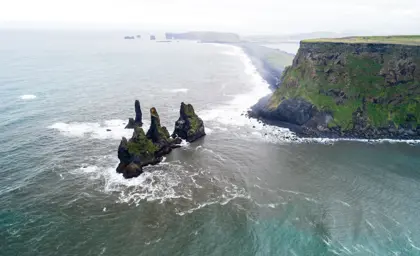 Aerial view of Reynisdrangar sea stacks along the rugged Icelandic coastline, captured from a tour highlighting the scenic beauty of the southern shores.