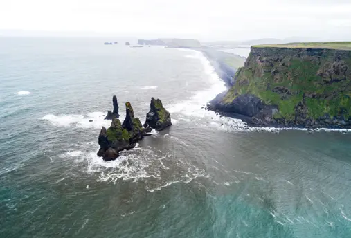 Aerial view of Reynisdrangar sea stacks along the rugged Icelandic coastline, captured from a tour highlighting the scenic beauty of the southern shores.