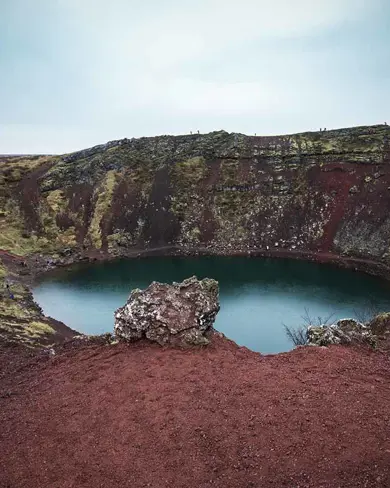 The vibrant red volcanic rock surrounding Kerid Crater Lake, Iceland.