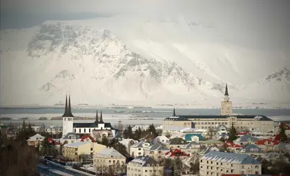A picturesque winter view of Reykjavik with snow-covered rooftops and mountains in the background.