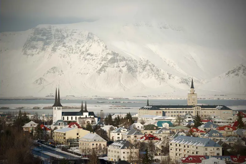 A picturesque winter view of Reykjavik with snow-covered rooftops and mountains in the background.