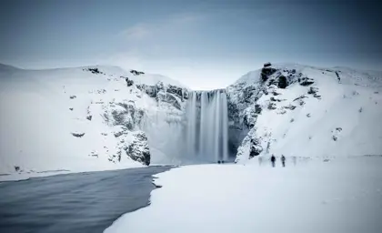 The majestic Skogafoss waterfall covered in snow and ice during winter in Iceland, creating a serene and powerful scene.