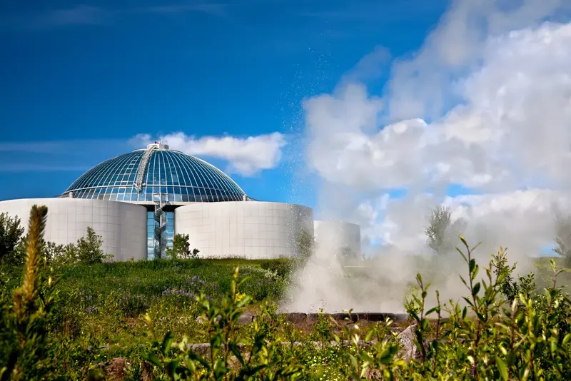 View of Perlan Museum and observation deck through a steam cloud and greenery.