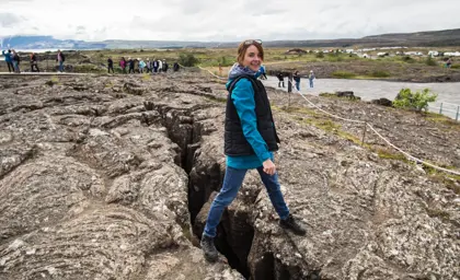 Smiling woman standing over a tectonic fissure at Þingvellir National Park, a UNESCO World Heritage site along Iceland’s Golden Circle route.