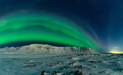 Green northern lights over snowy mountains in winter on northern lights tour with Travel Reykjavík.