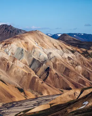 Panoramic view of the striking rhyolite mountains at Landmannalaugar, with layered colors and dramatic ridges under a blue sky, a famed Icelandic highland destination.