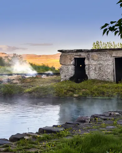 Secret Lagoon original stone bathhouse in gamla laugin in Flúðir, Iceland, surrounded by natural geothermal steam and wildflowers on a serene summer evening.