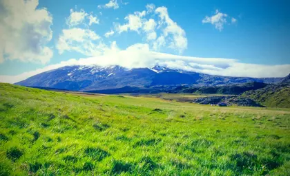Snow-capped Snæfellsjökull volcano in Iceland, with a vast green landscape in the foreground.