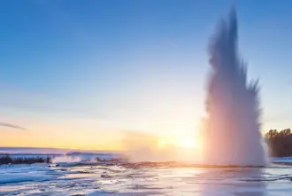 Geysir area on Golden Circle during winter Northern Lights Season with snow covered ground bathed in a golden sunset.