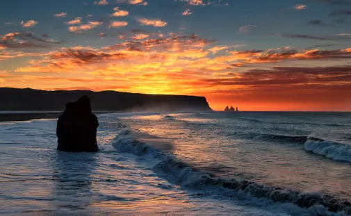 Reynisfjara at sunset on South Coast Day Tour from Reykjavík, seen with Reynisdrangar sea stacks at the horizon.
