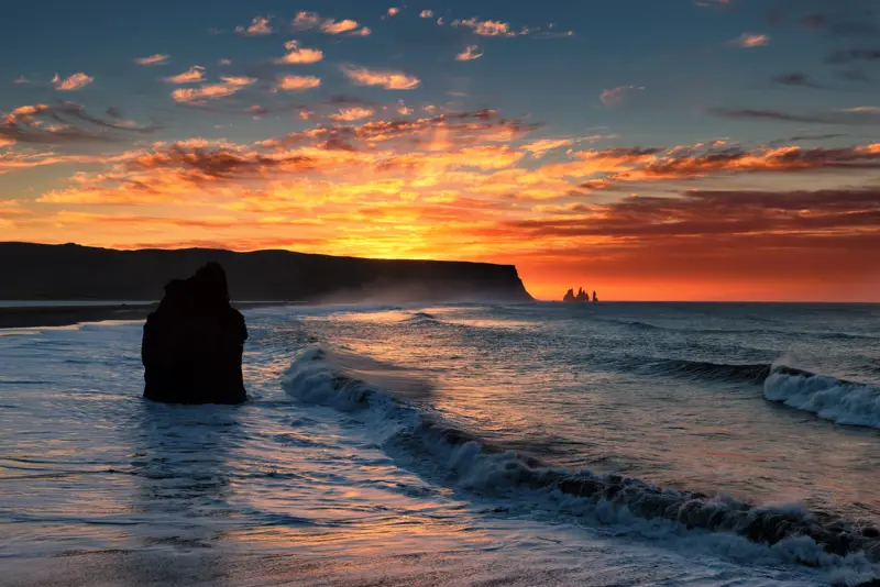 Reynisfjara at sunset on South Coast Day Tour from Reykjavík, seen with Reynisdrangar sea stacks at the horizon.